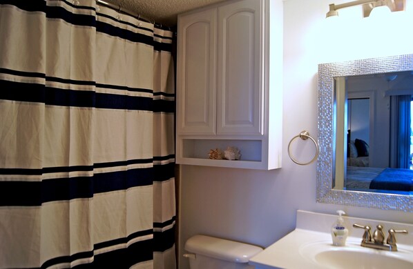 Un baño con cortina de ducha a rayas, un inodoro, un lavabo con espejo y una estantería con adornos.