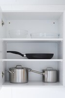 Un mueble de cocina con un bol de vidrio transparente, una sartén negra y dos ollas de acero inoxidable.