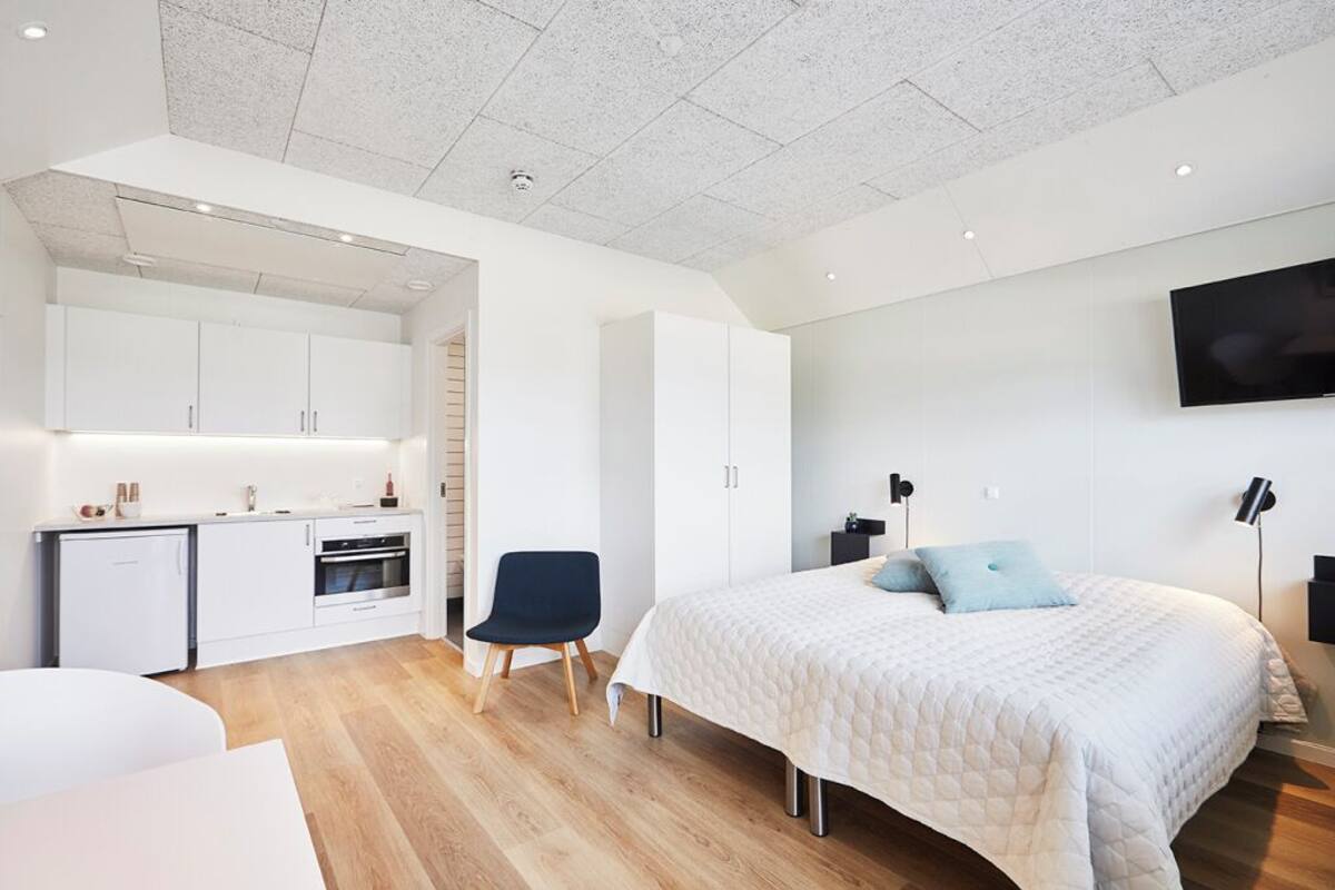 A modern bedroom with a large bed, a desk, and a kitchenette.