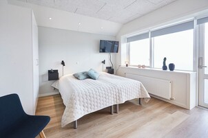 Un dormitorio moderno con una cama, un televisor montado en la pared, un ventanal con vistas y un radiador.