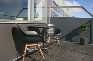 A rooftop terrace with a table and two chairs, a potted plant, and a view of a building in the background. - athome apartments (Aarhus)