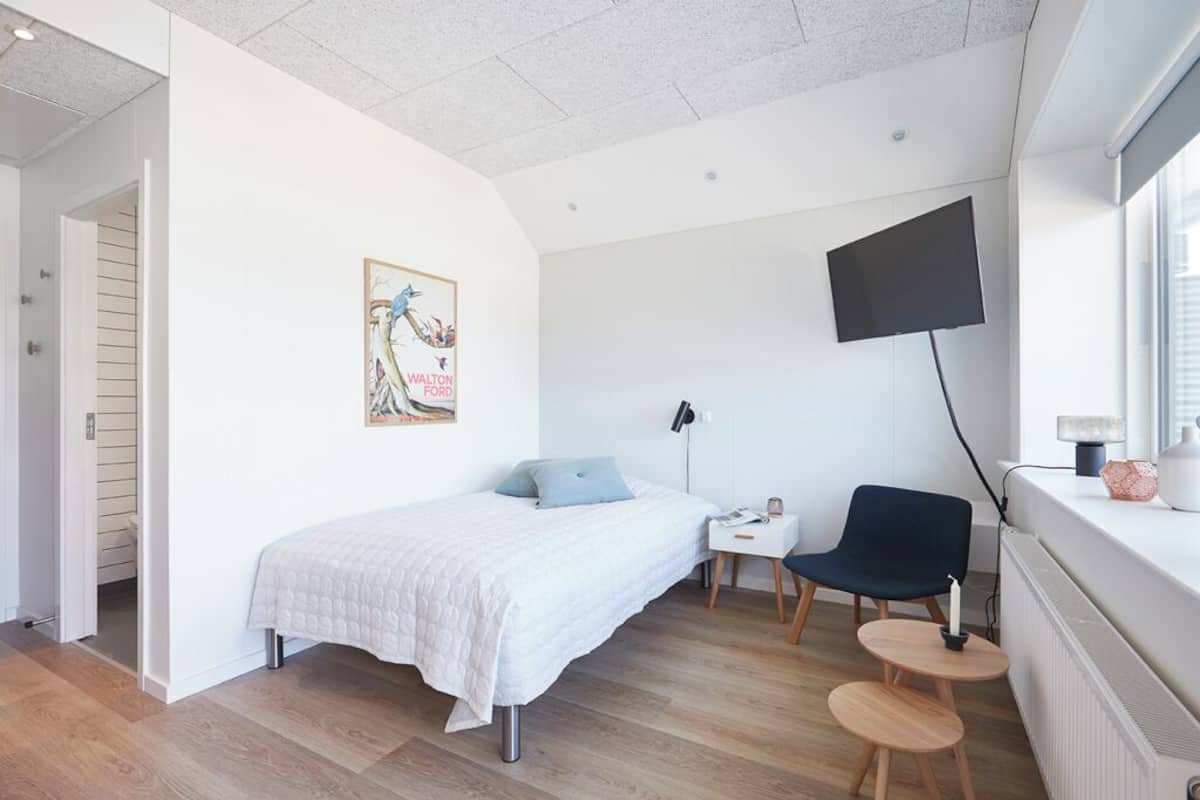 A modern bedroom with a bed, a desk, a chair, a TV, and a window.