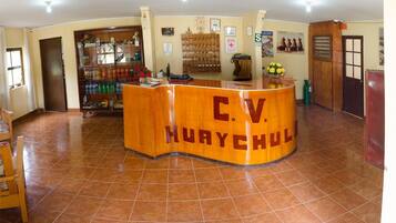 A reception desk labeled 'C.V. MURAYCHUL' with a tiled floor, a shelf with bottled water, and a clock on the wall.