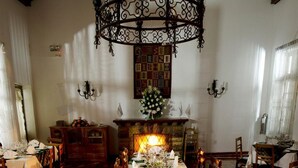 Un comedor con una gran mesa de madera preparada para una comida, una araña y una chimenea.