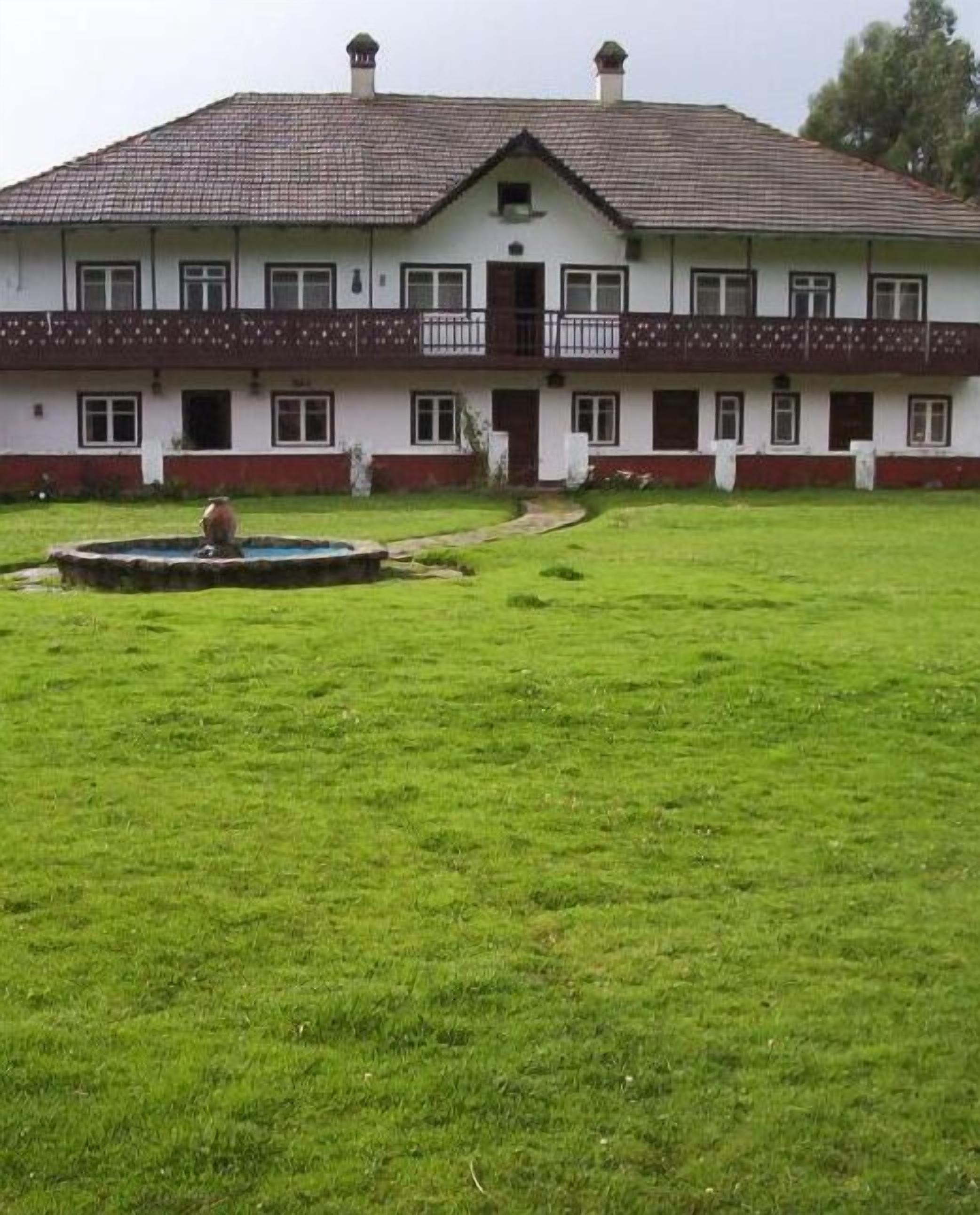 A large, two-story building with a symmetrical facade, a central entrance, and a small fountain in the front yard.