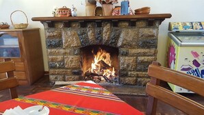 Una chimenea de piedra con fuego, una mesa de madera con mantel rojo y una silla.