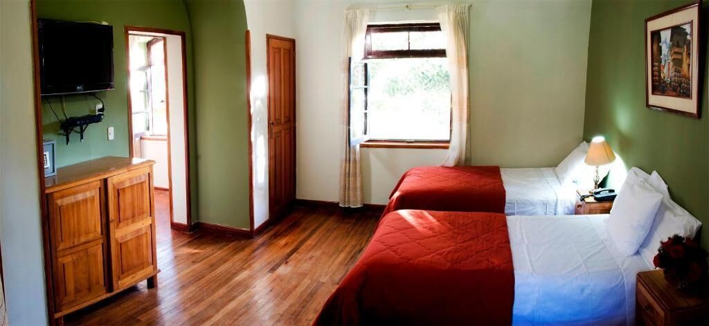 Una habitación con un armario de madera, una cama con ropa de cama roja y blanca, una mesita de noche con una lámpara y una ventana con cortinas.
