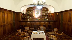 Comedor con una larga mesa, sillas de madera, un candelabro y una zona de bar con estantes llenos de botellas.