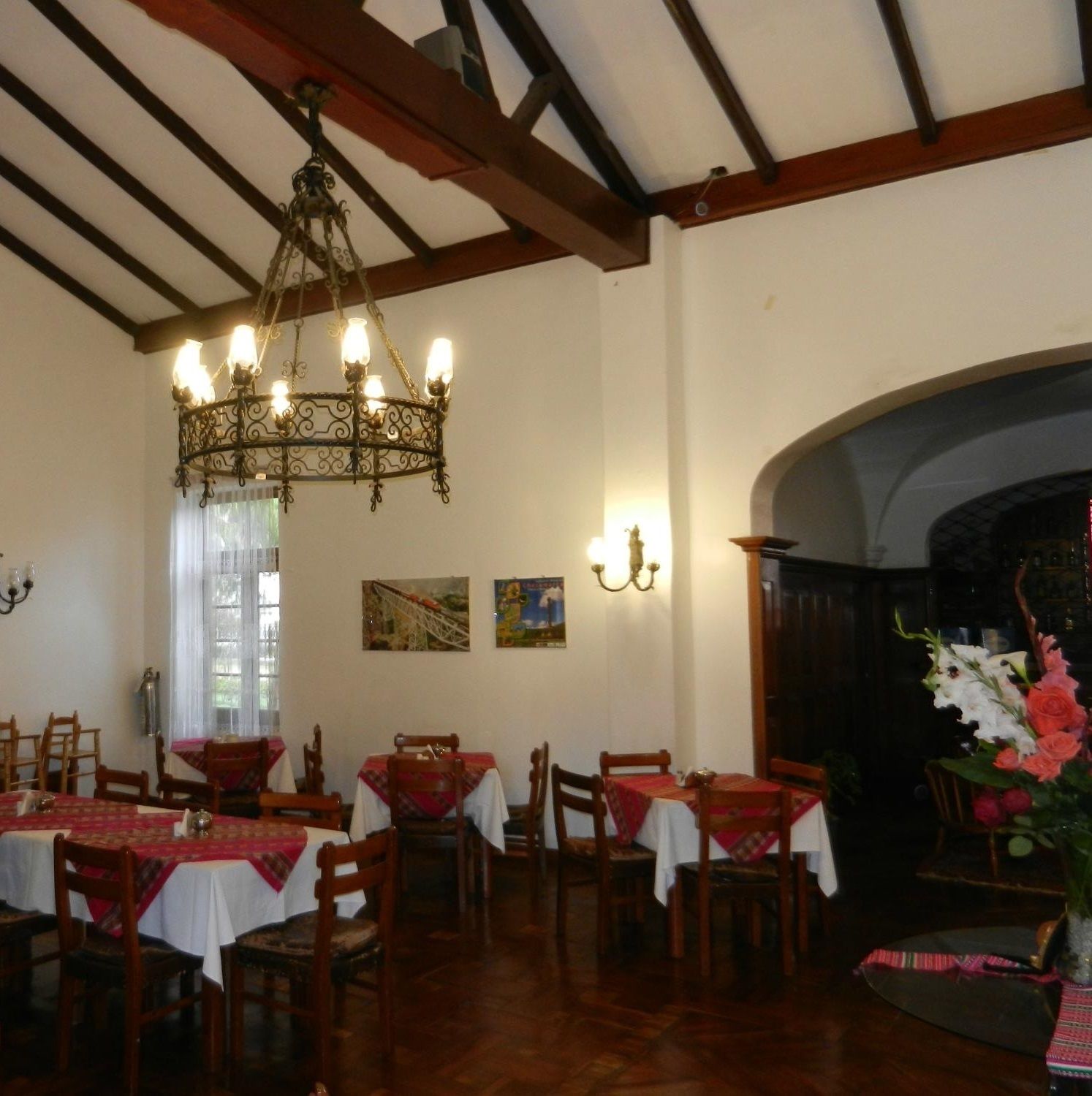 Un comedor con mesas y sillas de madera, una araña y obras de arte en las paredes.