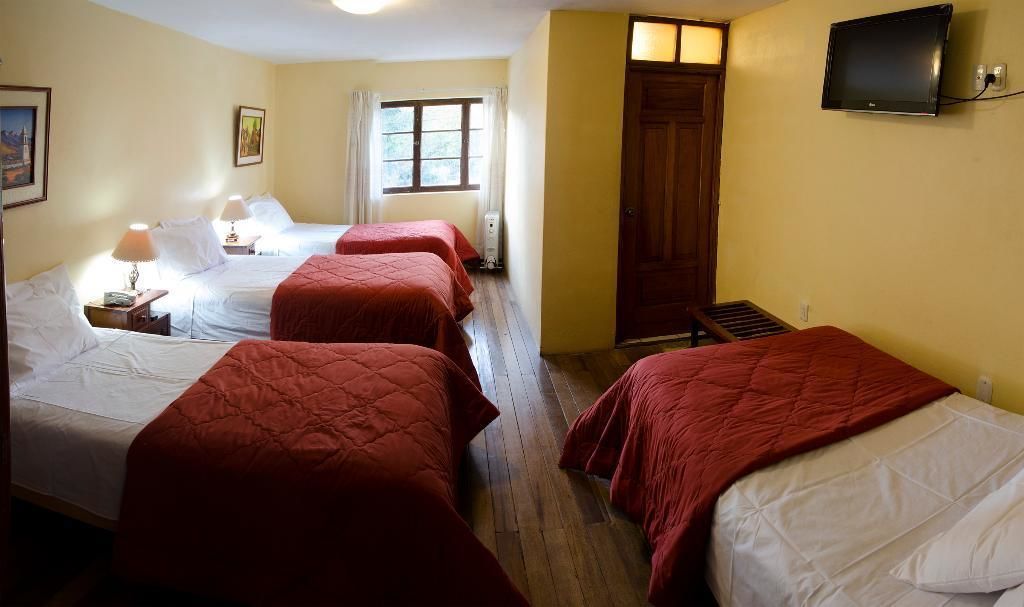 Habitación de hotel con tres camas, un televisor y una ventana con cortinas.
