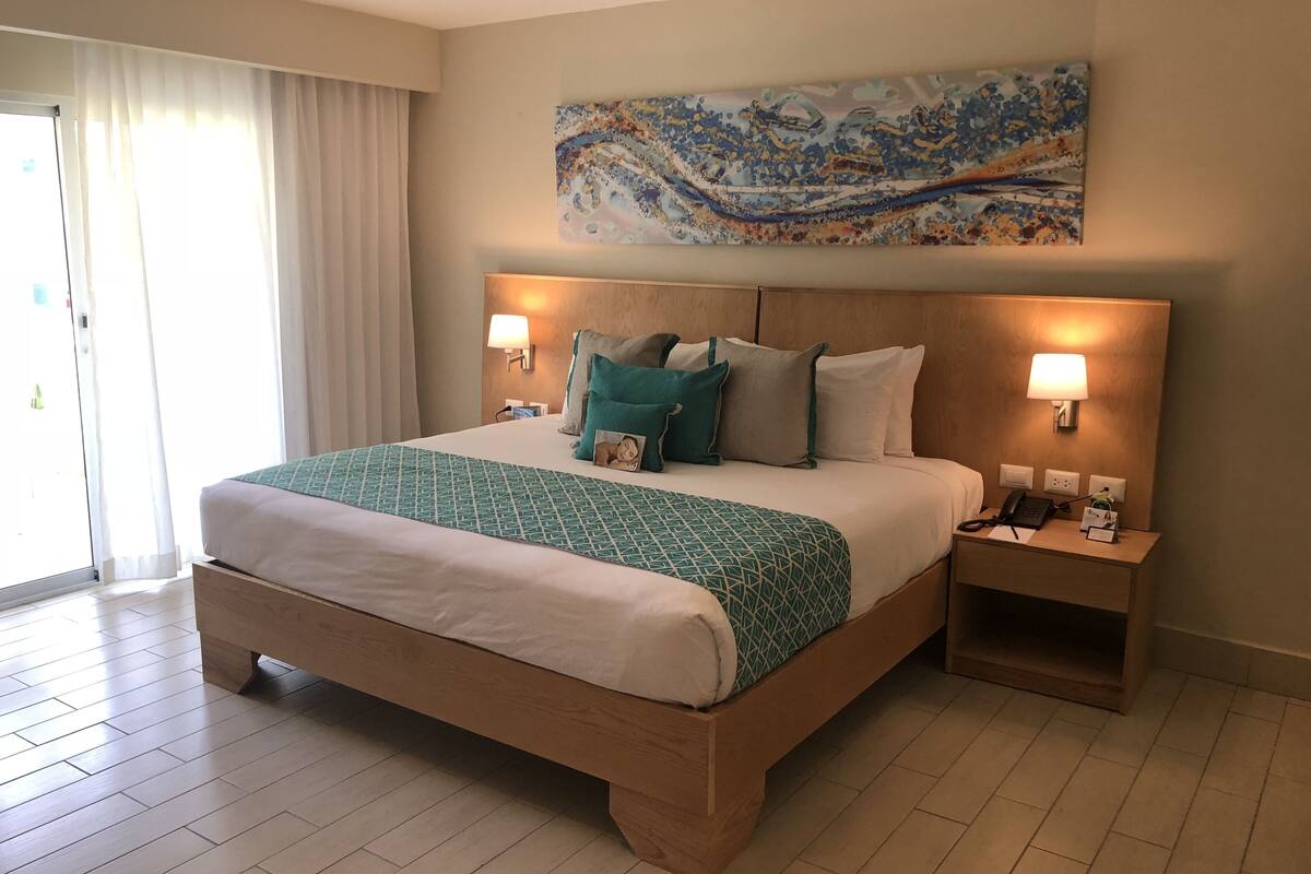 Une chambre d’hôtel avec un grand lit, deux tables de chevet, un tableau accroché au mur et une porte-fenêtre coulissante.