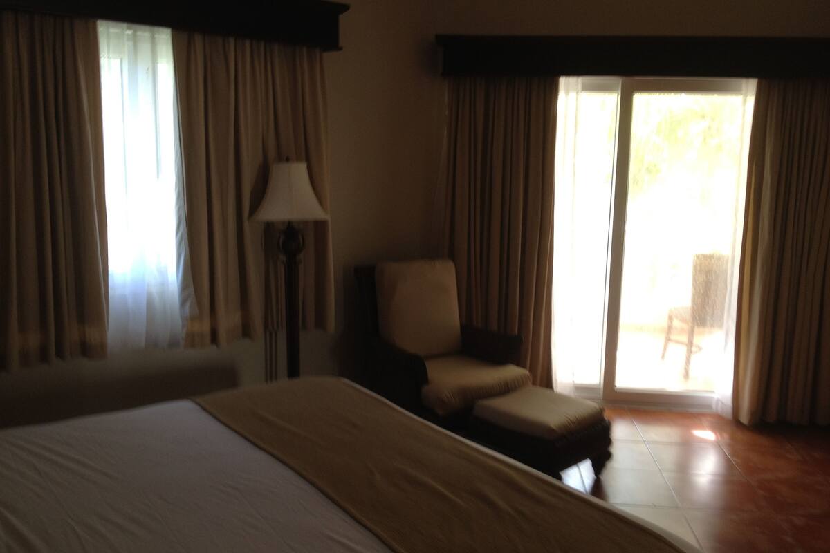 A hotel room with a large bed, a chair, a lamp, and a view of the outdoors through a sliding door.
