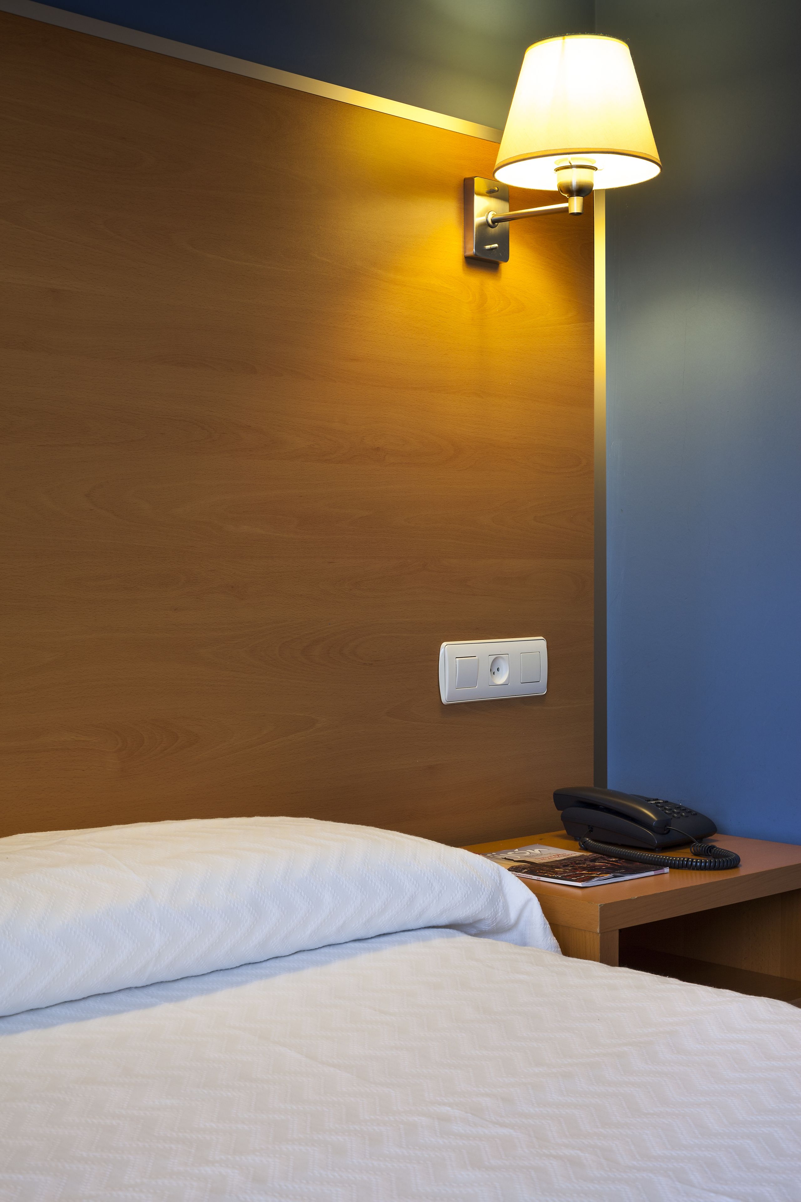 Una habitación de hotel con una cama, una mesita de noche con lámpara y un teléfono.