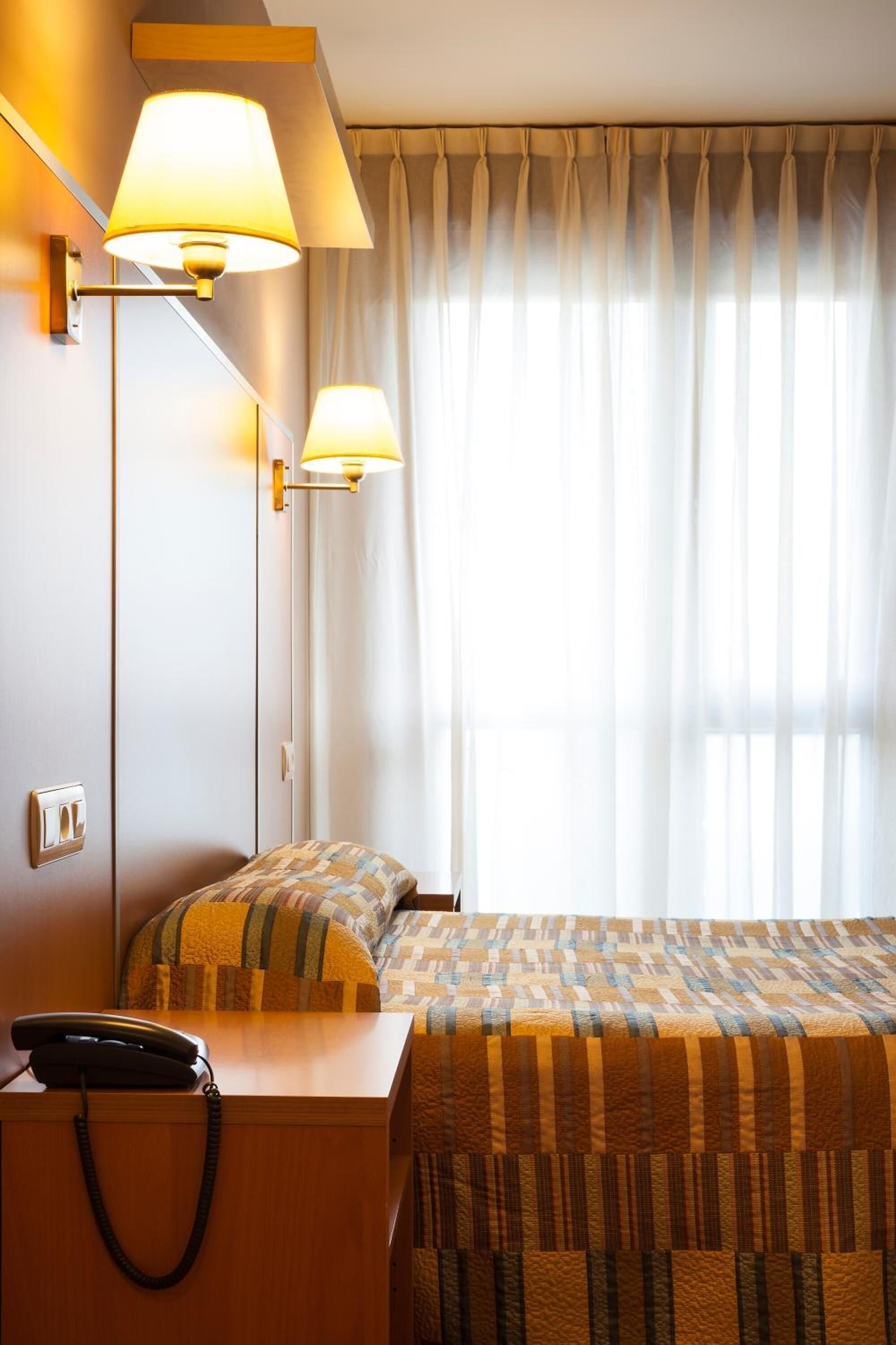 Una habitación de hotel con dos camas, un escritorio con teléfono y dos lámparas de pared.