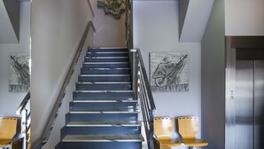 Una escalera con barandilla, una escultura en la pared y dos sillas.