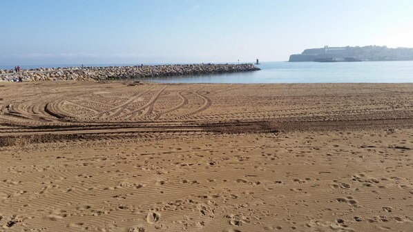 A sandy beach with tire tracks leading to a rocky breakwater. - Hotel La Polar (Gijon)
