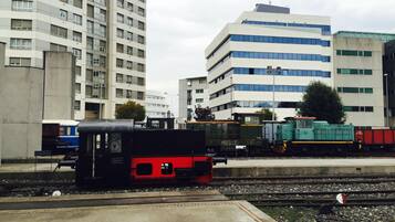 Uma estação de trem com várias plataformas e diversos trens, incluindo um trem vermelho e preto e um trem verde.