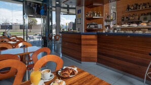Un café moderno con mobiliario de madera, una zona de bar con estantes llenos de botellas y vistas a la ciudad a través de amplios ventanales.