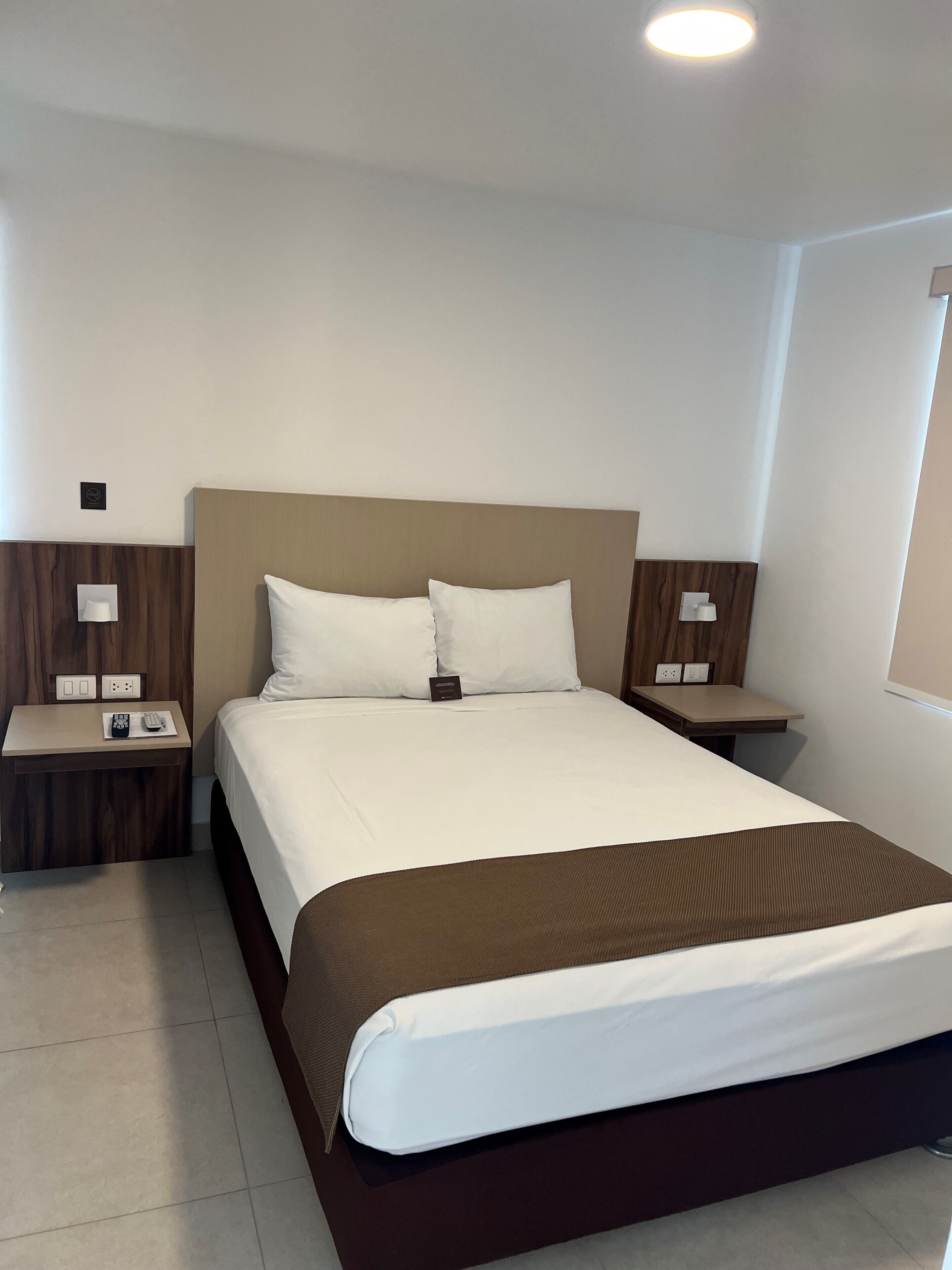 Una habitación de hotel con una cama grande, dos mesitas de noche y una lámpara de pared.