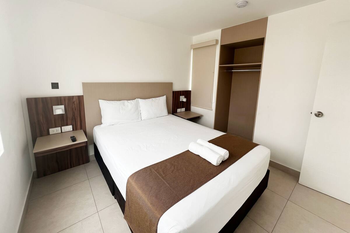 A hotel room with a large bed, a bedside table with a phone, a nightstand, a wardrobe, and a bathroom visible through an open door.