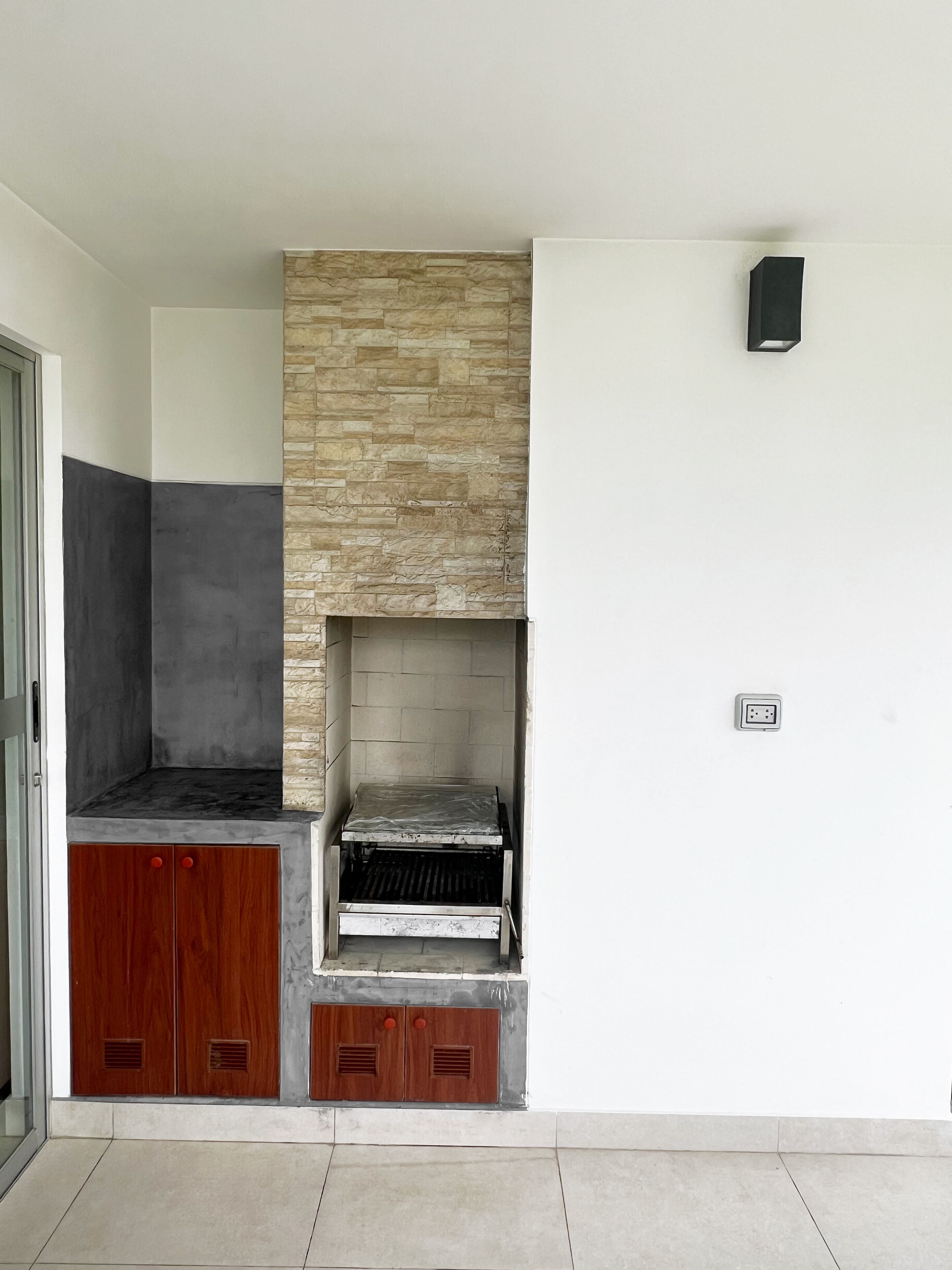A compact kitchen with a built-in grill, wooden cabinets, and a stone accent wall.