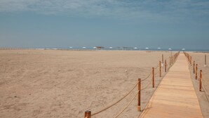 Una pasarela de madera que lleva a sombrillas de playa en una arena dorada.