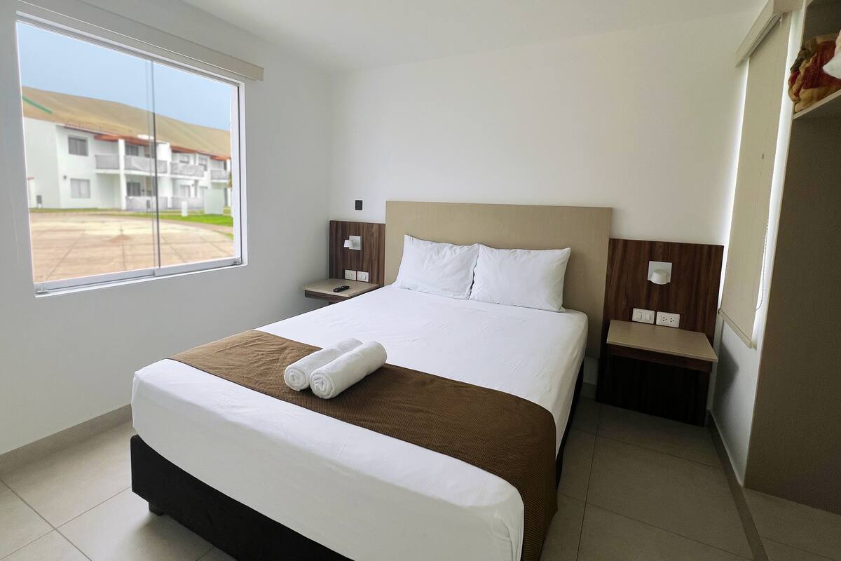 A hotel room with a large bed, a nightstand, a window, and a view of the outside.