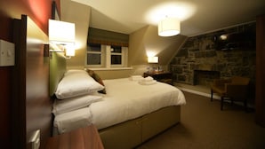 A bedroom with a large bed, a stone fireplace, and a television mounted on the wall. - The Portree Hotel (Portree)