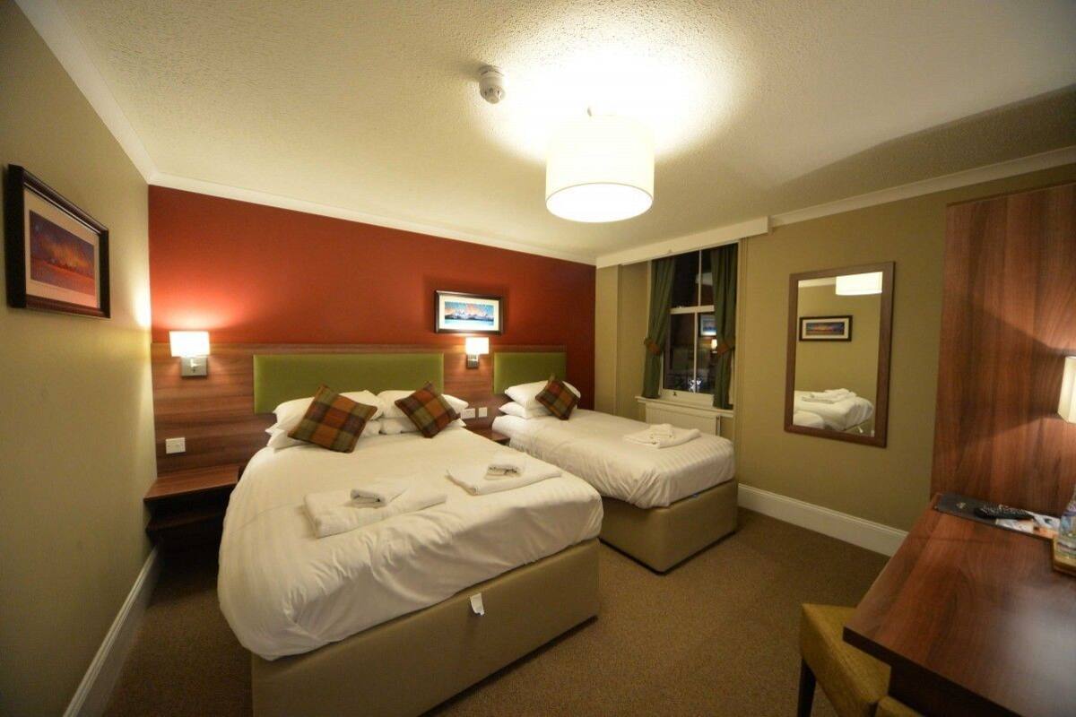 Ein Hotelzimmer mit zwei Betten, einem Schreibtisch, einem Spiegel und einem Fernseher.