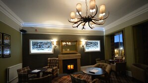 A cozy room with a fireplace, plaid carpet, and a chandelier. - The Portree Hotel (Portree)
