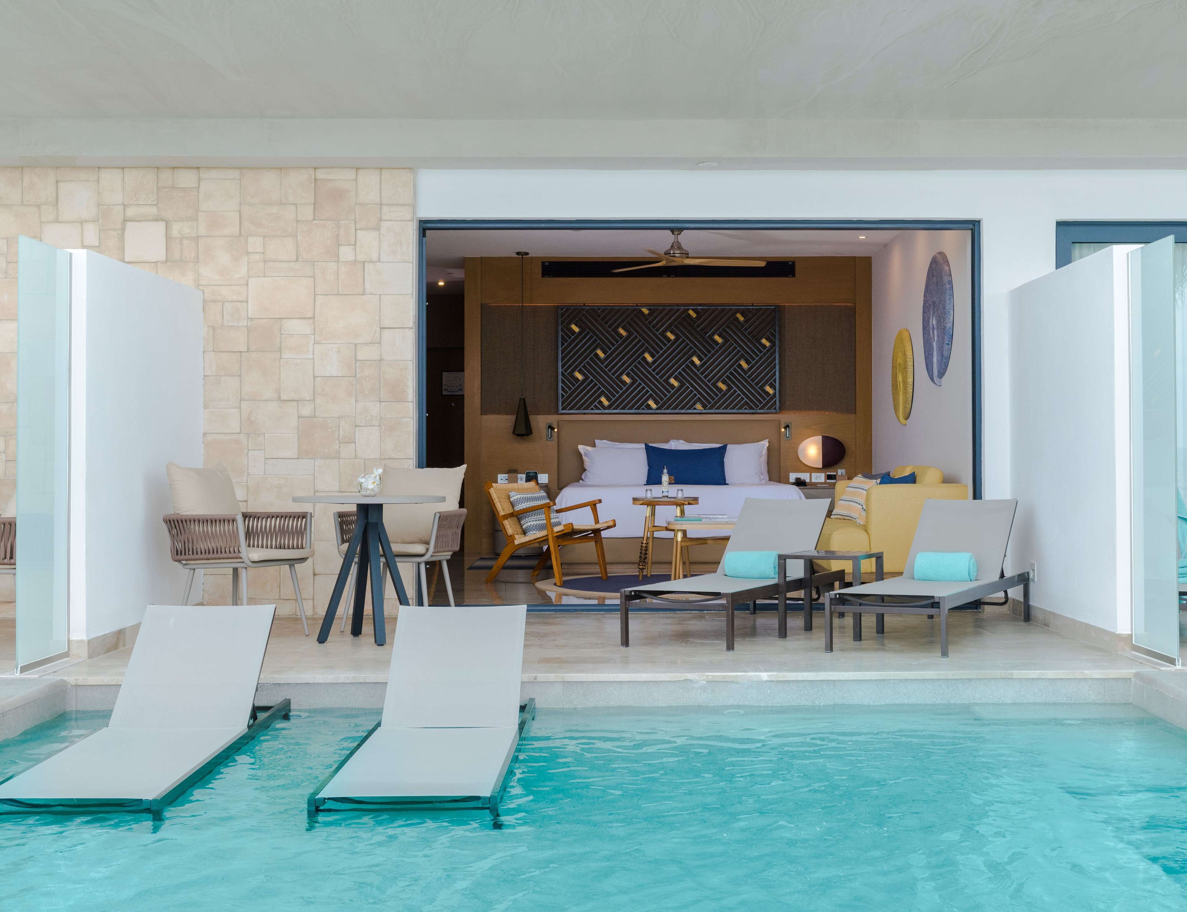 Une chambre d’hôtel équipée d’un lit, d’un bureau, d’un ordinateur portable, d’une petite table et d’un espace piscine avec des chaises longues.