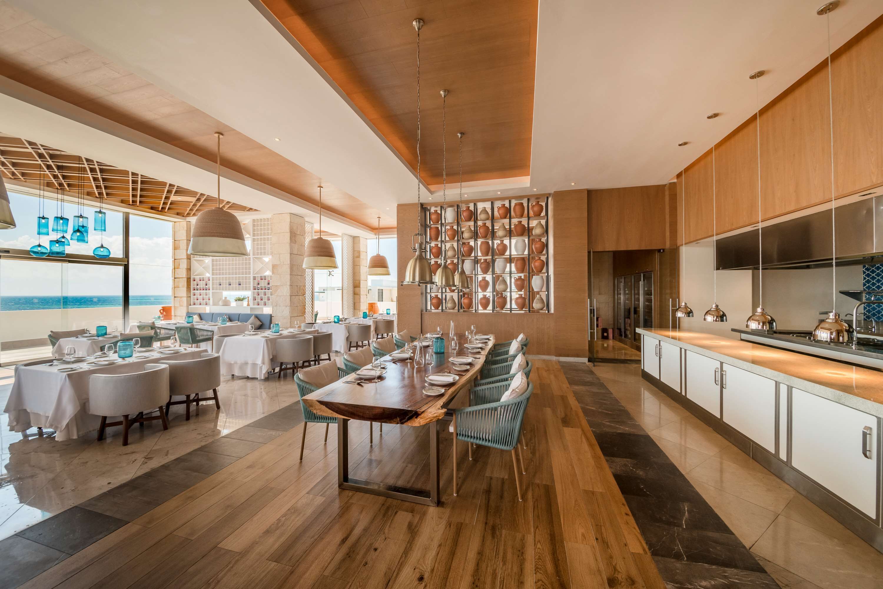 Un espace repas moderne avec une longue table en bois, des chaises bleues et un mur décoré de poteries.