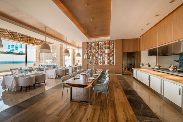 A modern dining area with a long wooden table, blue chairs, and a wall of decorative pottery.