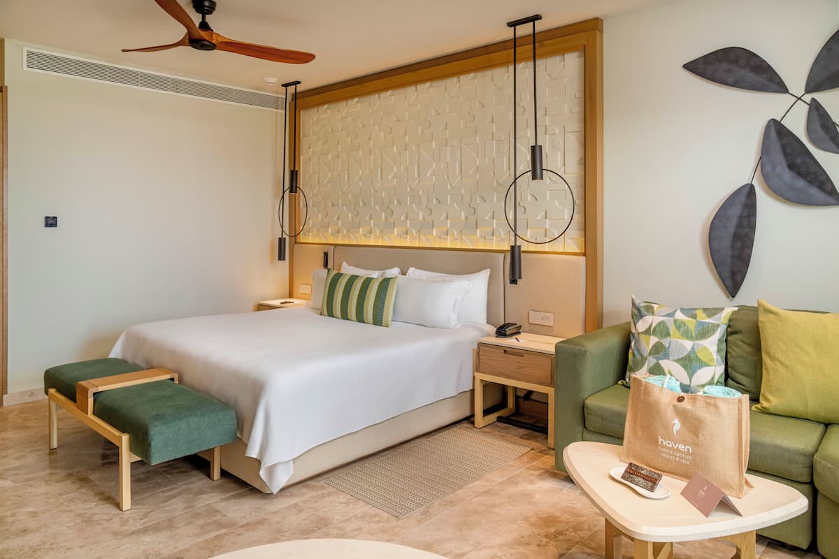 A hotel room with a bed, bedside tables, a green sofa, a coffee table, and a ceiling fan.