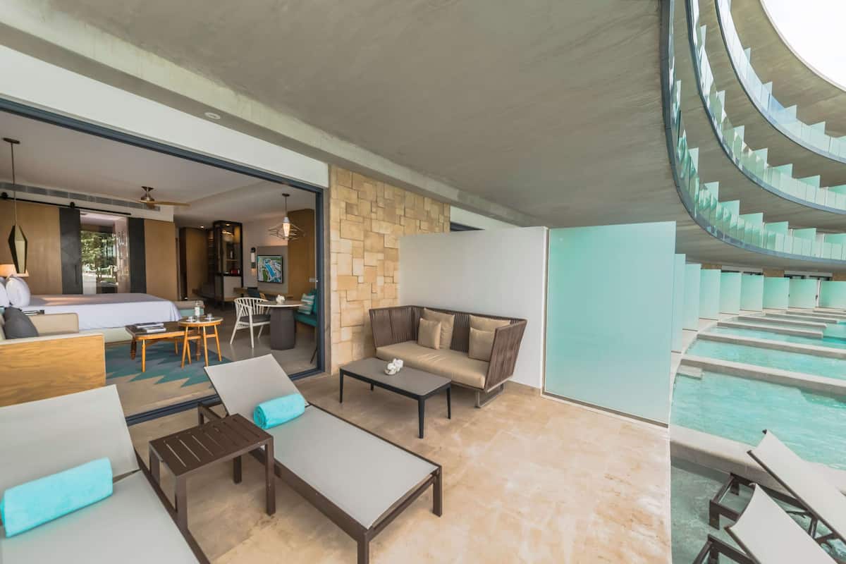 A modern hotel room with a pool, a dining area, and a living room with sofas and a coffee table.