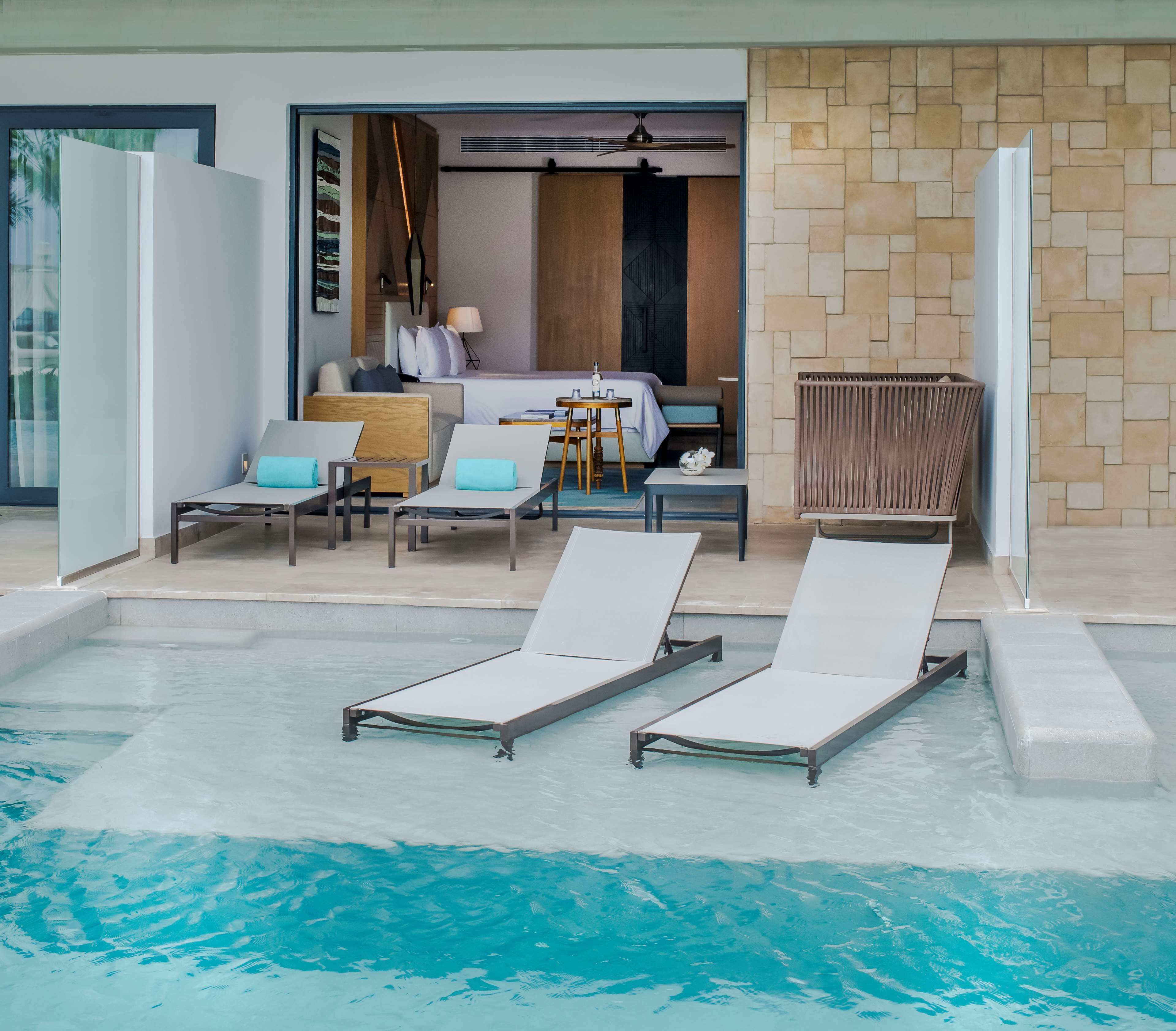 A pool area with lounge chairs and a bedroom with a bed, a desk, and a chair.