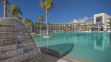 A large swimming pool with palm trees and a modern hotel building in the background.