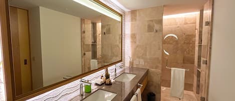 A modern bathroom with two sinks, a large mirror, and a walk-in shower.