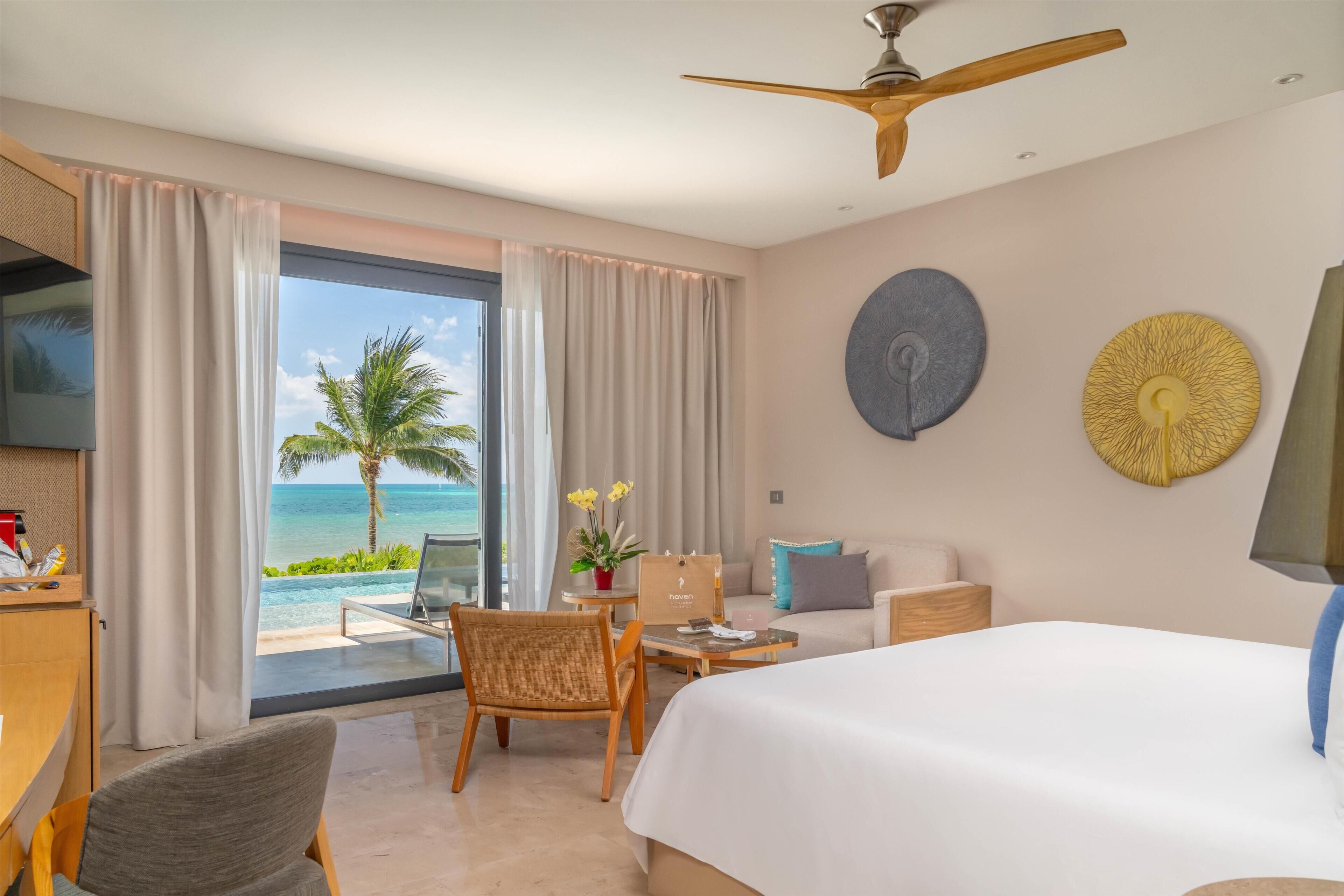 A hotel room with a bed, a desk, a chair, a table, and a view of the ocean.