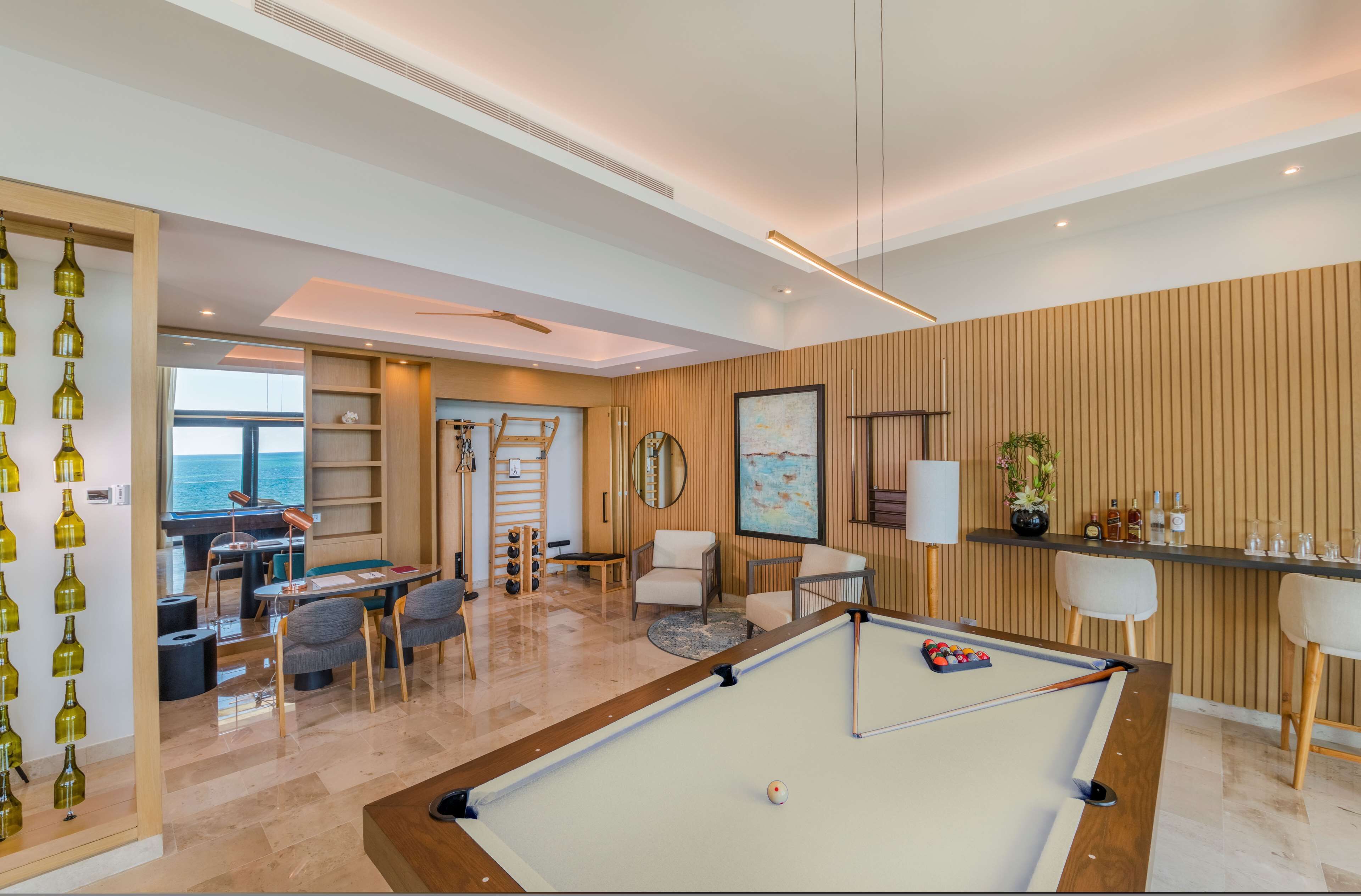 Uma sala de estar moderna com mesa de bilhar, assentos confortáveis, um bar e vista para o mar.