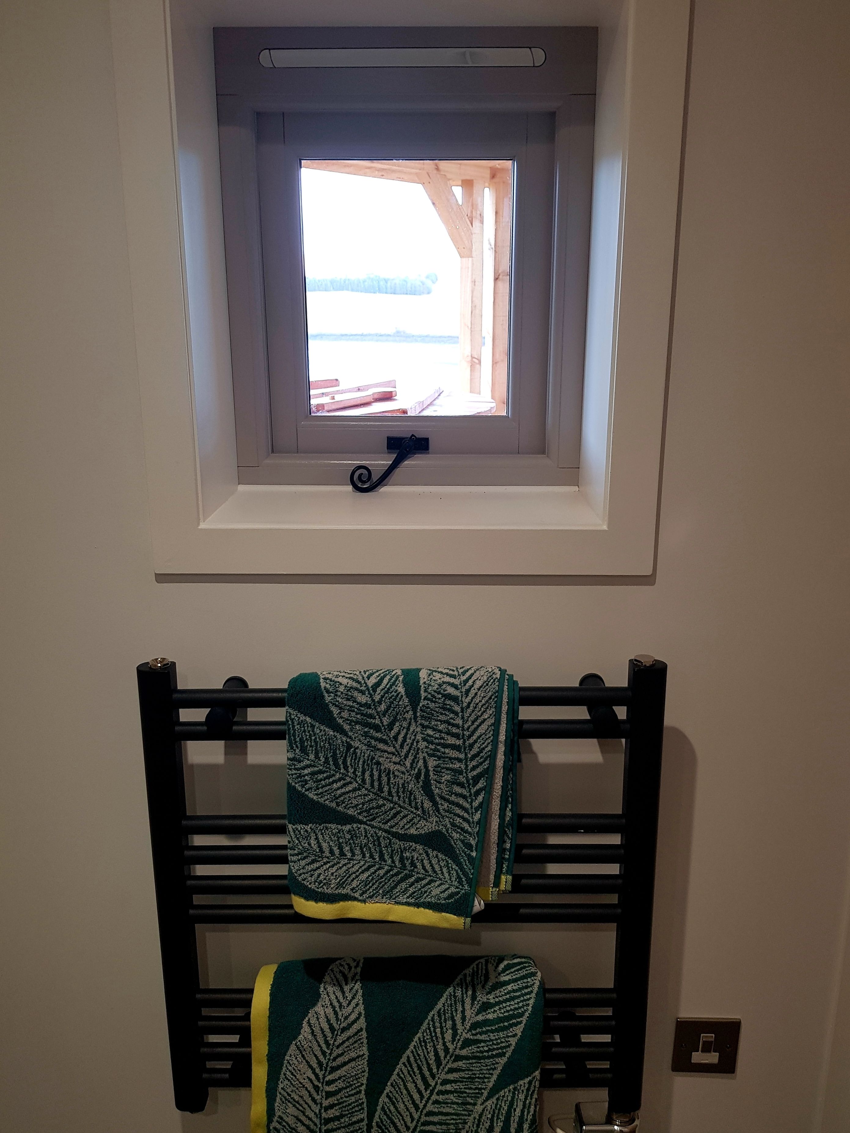 A room with a small window, a towel rack with a towel, and a light switch on the wall.