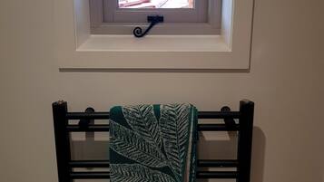 A room with a small window, a towel rack with a towel, and a light switch on the wall.