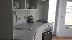 A kitchen with white cabinetry, a built-in oven, and a window providing a view of the outdoors. - Skye Cabins (Skeabost)