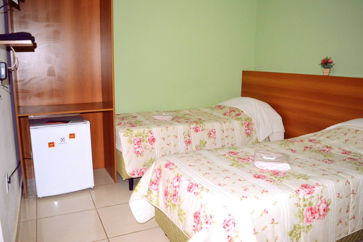 Una habitación con dos camas, un refrigerador pequeño y un cabecero de madera.