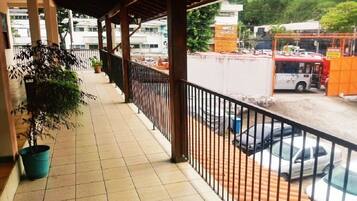 A covered balcony with tiled flooring, a potted plant, and a view of parked cars and a bus on the street.