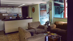 Zona de recepción con mostrador, dos sillones, una mesita con revistas y una ventana que ofrece vistas a una escalera.