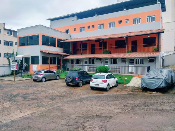 Un hotel de varios pisos con recepción, estacionamiento y una zona de estar al aire libre techada.