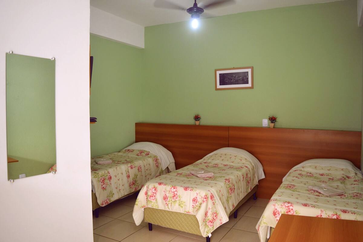 Una habitación con dos camas individuales, un cabecero de madera, un cuadro pequeño en la pared y un ventilador de techo.