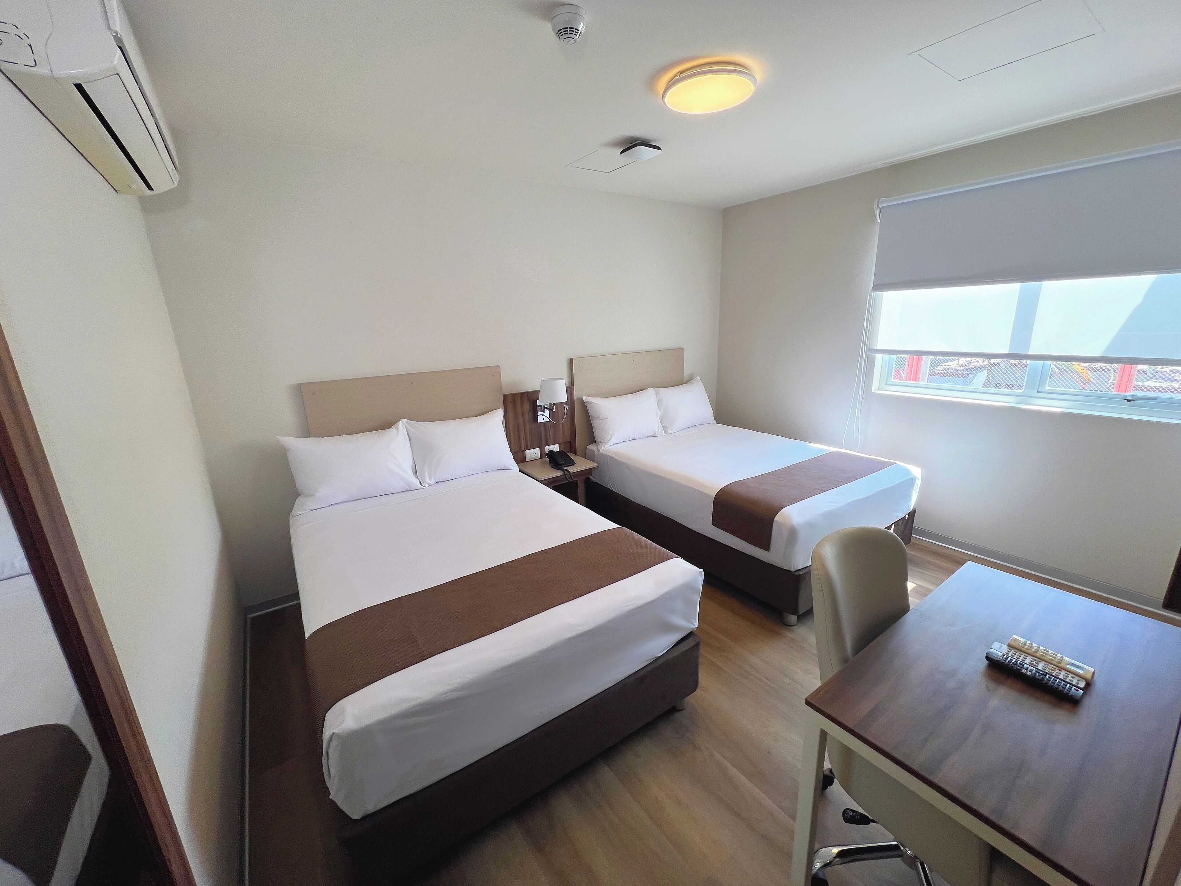 A hotel room with two beds, a desk, and a window.
