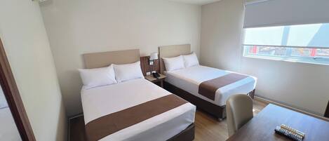 A hotel room with two beds, a desk, and a window.